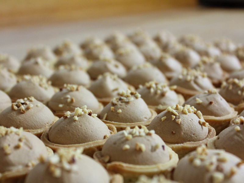 Reihen von Tartelettes mit Mousse-Kuppeln und Nusskrokant in der Backstube