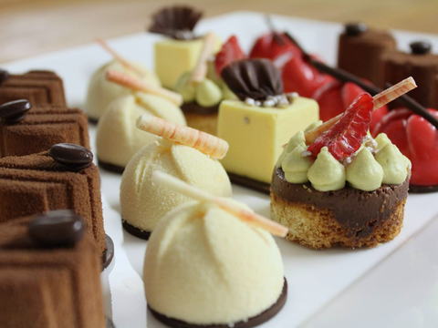 Platte mit Petits Fours: Mousse-Kuppeln, Fruchtgelee-Törtchen, Schokoladenwürfel und Pistaziencreme